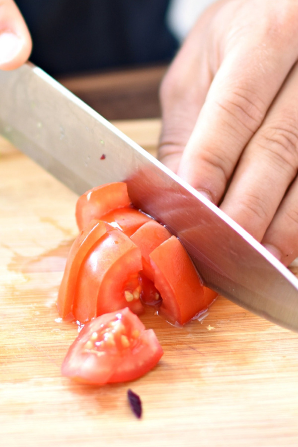A person cutting a tomato with a large knife. 