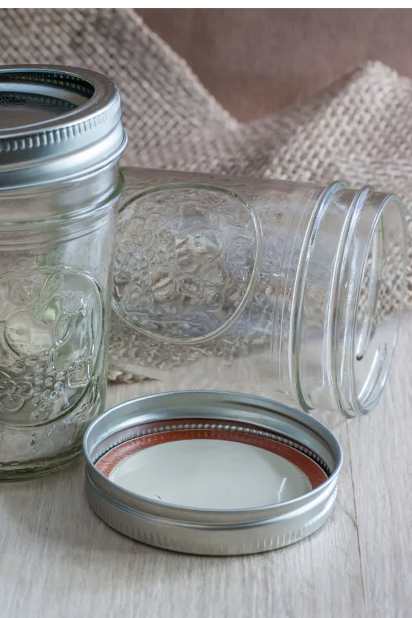 Two canning jars with the lids on a wooden table.