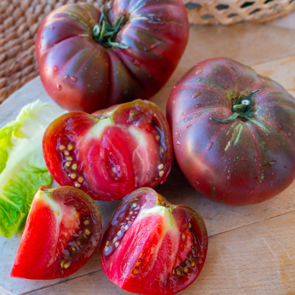 Black Krim tomatoes sliced and whole sitting on a plate.
