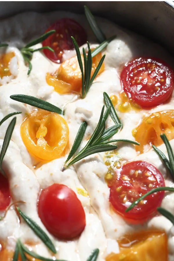 tomatoes and rosemary on top of focaccia bread dough