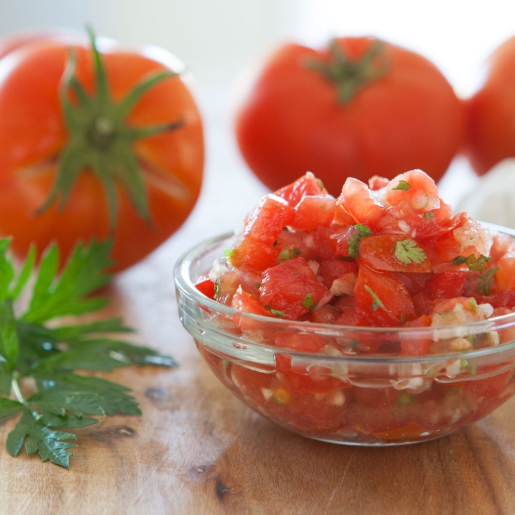 A bowl of fresh salsa in front of faded tomatoes