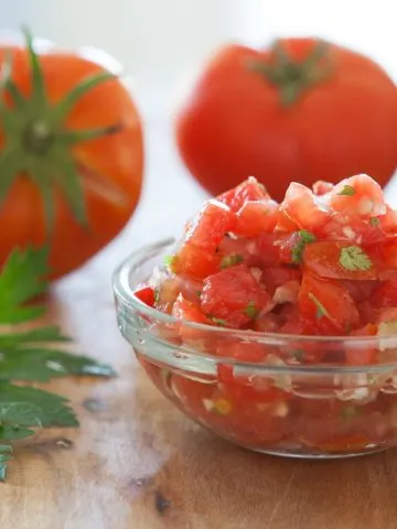 A bowl of fresh salsa in front of faded tomatoes